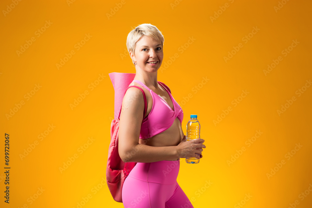 Fitness woman holding yoga mat in backpack isolated on yellow background. Fitness woman holding yoga mat in backpack isolated on yellow background.