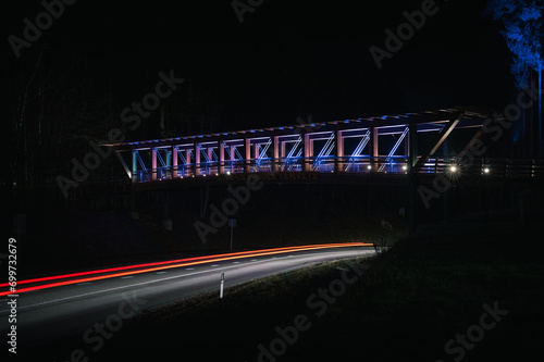 Obraz na płótnie Colorful footbridge leading over a highway at night time. Light trails from car lighting up the road. w salonie
