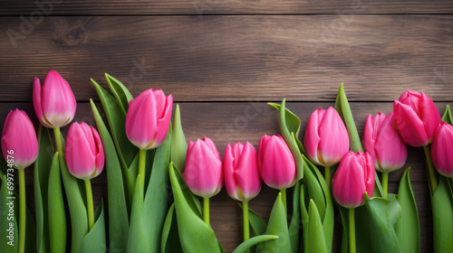 Vibrant pink tulips with green stems and leaves, lined up against a wooden background.