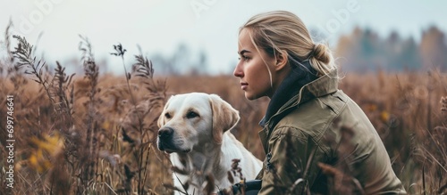 A young woman and her white labrador retriever in field training.