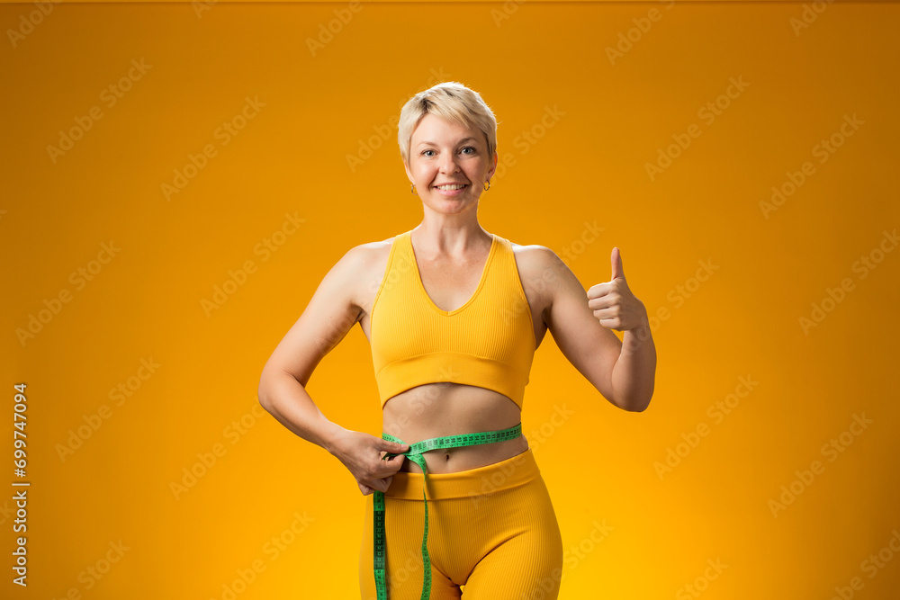 Fitness woman with measure tape isolated on yellow background. Weight loss and healthcare concept Fitness woman with measure tape isolated on yellow background. Weight loss and healthcare concept