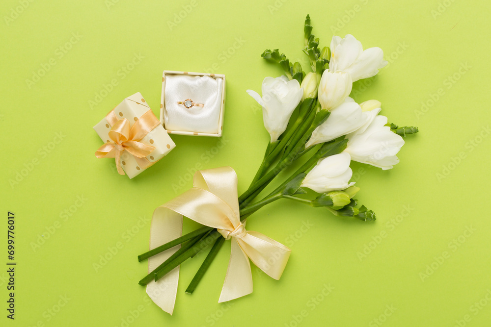 White freesia flower and gift box with diamond ring on color background, top view White freesia flower and gift box with diamond ring on color background, top view