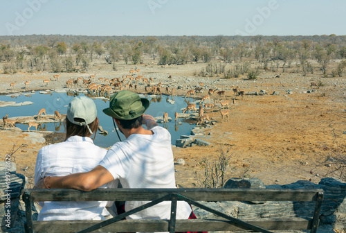 Rear view of young couple observing animals in African savannah - travel concept