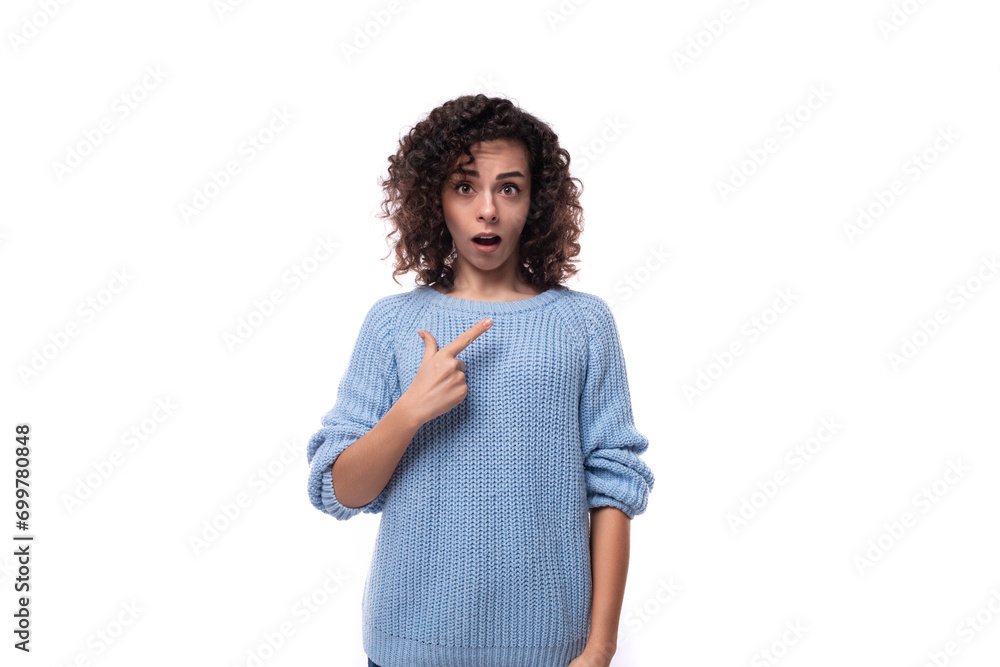 surprised young brunette woman with curls dressed in a blue knitted sweater points her hand to the side. advertising concept surprised young brunette woman with curls dressed in a blue knitted sweater points her hand to the side. advertising concept