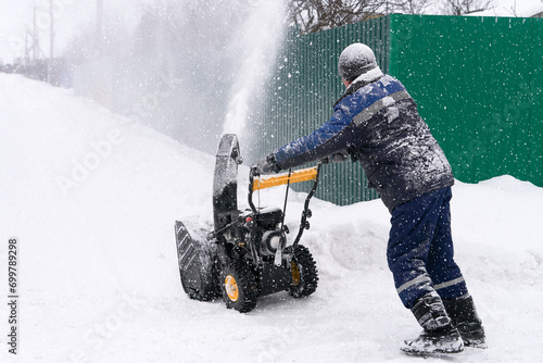 A man uses a compact snow blower to clear snow from a neighborhood after a snowstorm in the suburbs. Copy space. photo