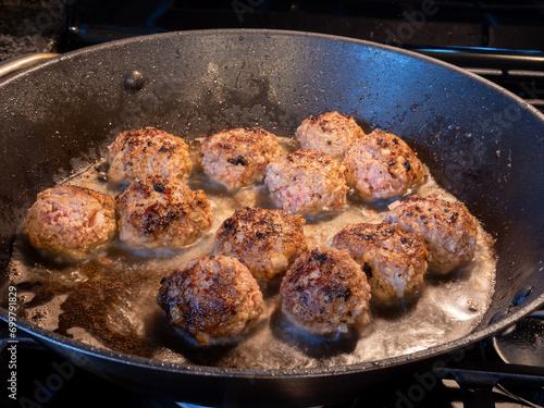 Closeup view of golden brown meatballs frying in butter in a frying pan.