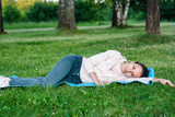 Portrait of dreamful woman lying on green grass in park
