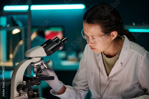 Female lab assistant putting piece of meat under magnification of microscope for scientific analysis