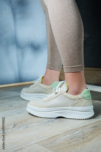 Close-up of female legs in leather sneakers on feet. Modern seasonal collection of stylish sneakers. Women s fashion.