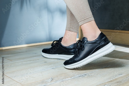 Black women's sneakers. Collection of women's leather shoes. Female legs in leather black casual sneakers. Stylish women's sneakers.