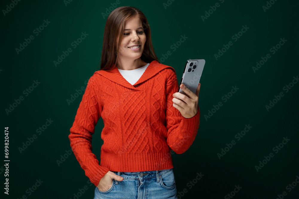 Pretty young woman studying news in smartphone on dark green background