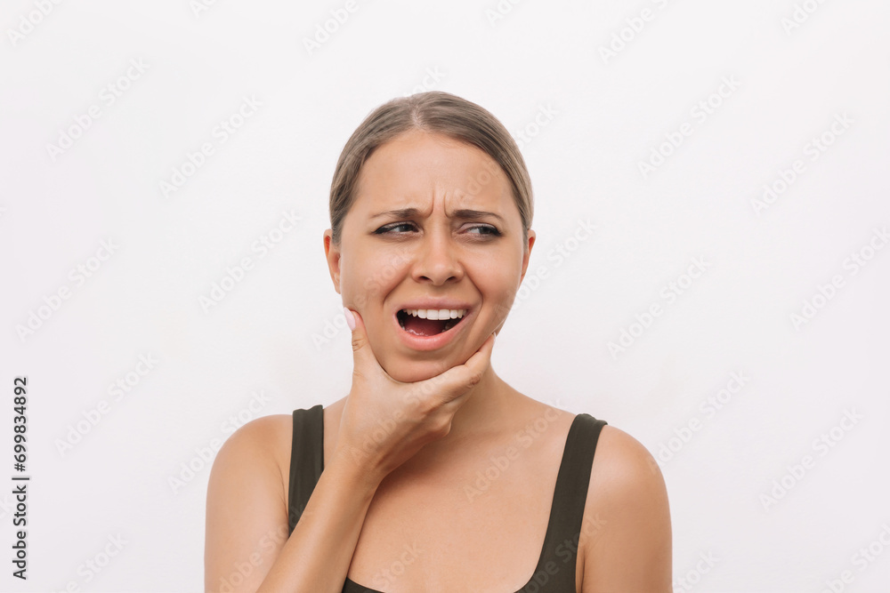 Young woman suffering from jaw pain holding her chin isolated on light background. Inflammation of cervical lymph nodes, Diseases of ENT organs, facial, trigeminal nerve, toothache, dislocation of jaw Young woman suffering from jaw pain holding her chin isolated on light background. Inflammation of cervical lymph nodes, Diseases of ENT organs, facial, trigeminal nerve, toothache, dislocation of jaw