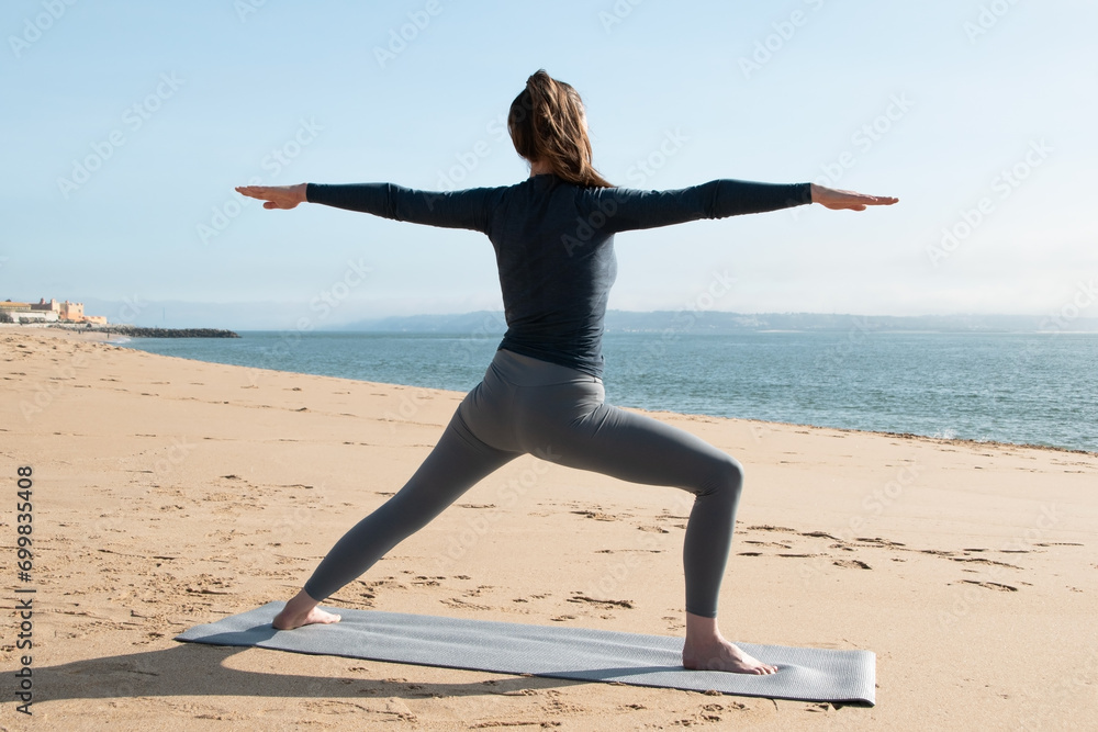 Fototapeta premium Young woman practicing yoga on the beach by the sea on a sunny day