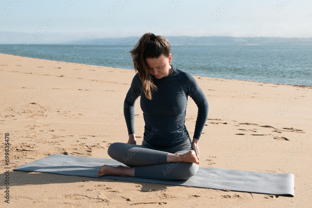 Fototapeta premium Full length portrait of a young woman practicing yoga on the beach.