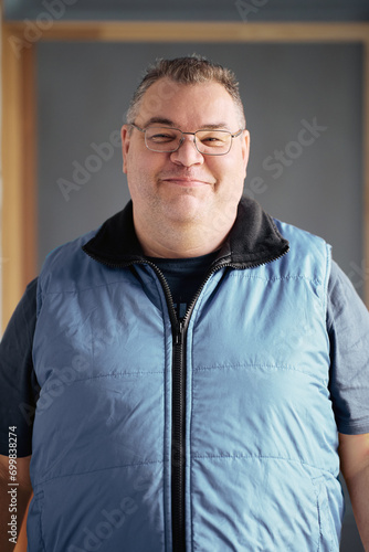 Heavily built European man wearing glasses with short haircut stands grinning.