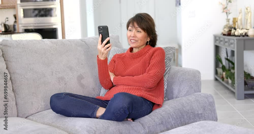 Mature stylish woman enjoying Facetime zoom talking on mobile cell phone relaxing sitting on home couch. Mature stylish woman enjoying Facetime zoom talking on mobile cell phone relaxing sitting on home couch.