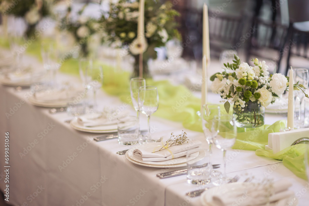 Stylish elegant table setting for festive dinner. The chairs and table for guests, served with cutlery, greenery flowers and crockery and covered with a white tablecloth. Catering on Wedding. Banquet.