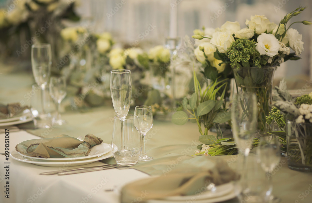 Stylish elegant table setting for festive dinner. The chairs and table for guests, served with cutlery, greenery flowers and crockery and covered with a white tablecloth. Catering on Wedding. Banquet. Stylish elegant table setting for festive dinner. The chairs and table for guests, served with cutlery, greenery flowers and crockery and covered with a white tablecloth. Catering on Wedding. Banquet.