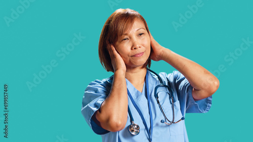 Competent nurse tormented by extreme noise while at work  close up. Healthcare employee covering ears with hands  bothered by rowdy surrounding sounds  isolated over studio background