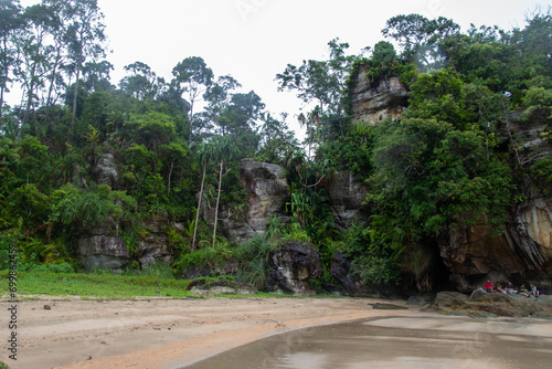 Принти на полотні A lush green forest and rock formations along a sandy beach.