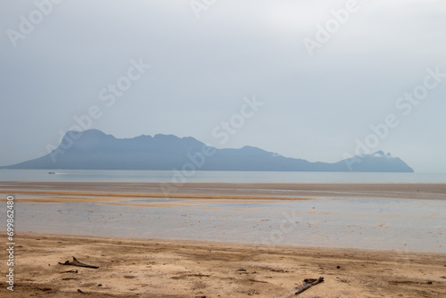 A serene beach view with distant mountains shrouded in haze.