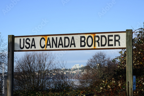Text sign in black capital letters on white background for USA Canada Border with rust marks from metal frame
