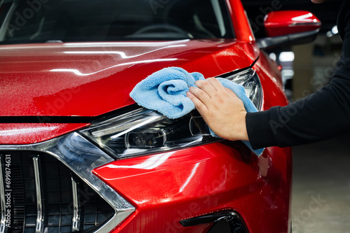 A man wipes the headlights of a red car with a microfiber cloth.