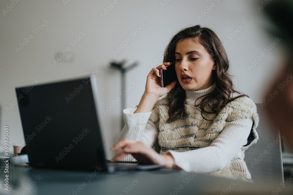 Brunette woman discussing with client via phone call while working on lap top at the office. Brunette woman discussing with client via phone call while working on lap top at the office.