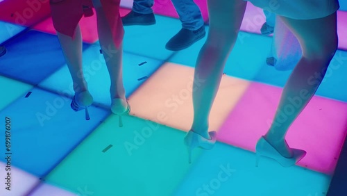 Girls in evening dresses and shoes with heels dance on luminous square disco floor. Vintage disco party with dancing girls. Party at nightclub in style of 80s. Colored flashing floor in nightclub