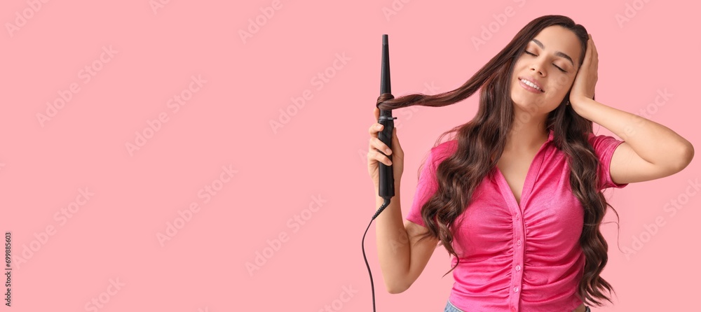 Beautiful young woman using curling iron on pink background with space for text Beautiful young woman using curling iron on pink background with space for text