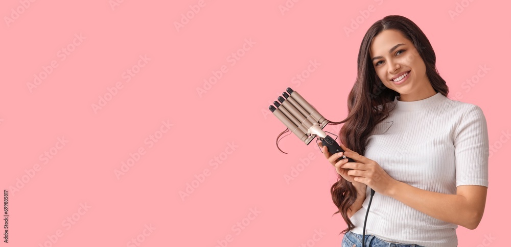 Beautiful young woman with curling iron on pink background with space for text Beautiful young woman with curling iron on pink background with space for text