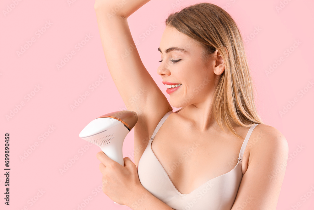 Beautiful young woman epilating her armpits with modern photoepilator on pink background Beautiful young woman epilating her armpits with modern photoepilator on pink background