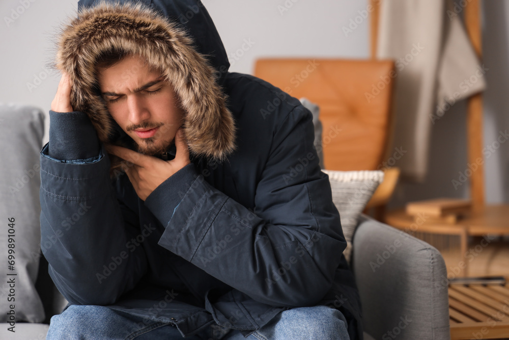 Fototapeta premium Frozen young man in puffer jacket at home