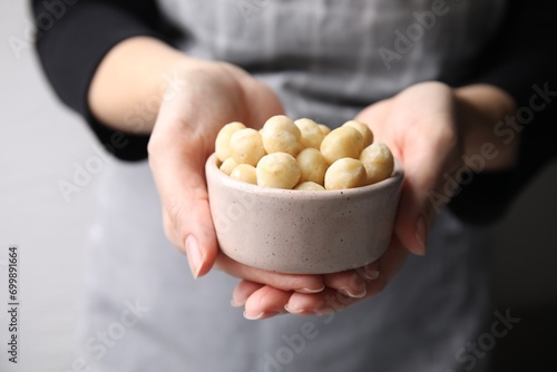 Woman holding bowl with delicious macadamia nuts, closeup photo