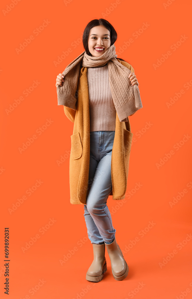 Beautiful young Asian woman in warm scarf on orange background Beautiful young Asian woman in warm scarf on orange background