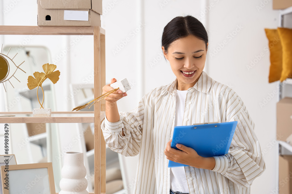 Female Asian seller with home decor and clipboard in warehouse store Female Asian seller with home decor and clipboard in warehouse store