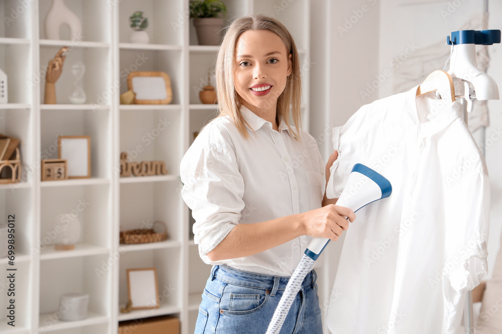 Fototapeta premium Pretty young woman steaming clothes with modern steamer at home