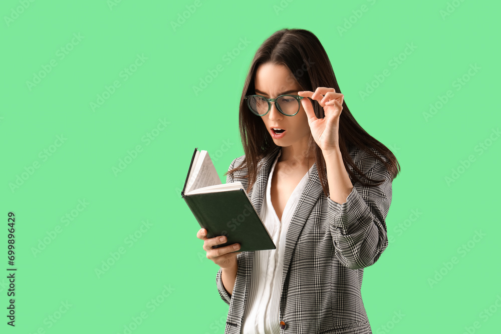 Shocked young businesswoman in eyeglasses reading book on green background Shocked young businesswoman in eyeglasses reading book on green background