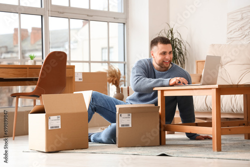 Young man with parcels using laptop at home