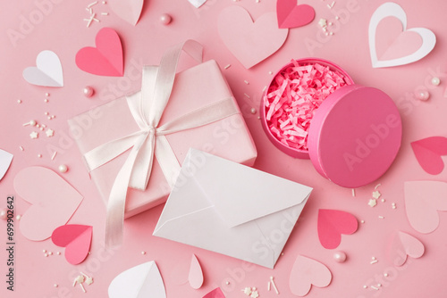 Envelope with gift boxes, paper hearts and decor on pink background. Valentine's Day celebration