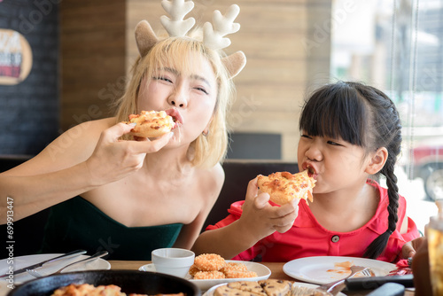 Happy mother and daughter Having Pizza in a Restaurant. Happy family craving for fast food meal