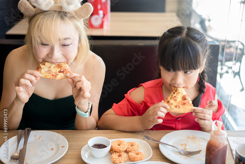 Happy mother and daughter Having Pizza in a Restaurant. Happy family craving for fast food meal