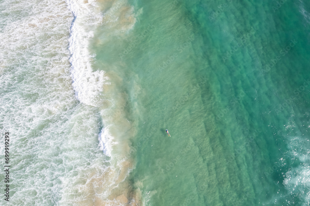 A surfer swims back to the shore viewed from above.