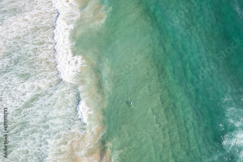 A surfer swims back to the shore viewed from above.