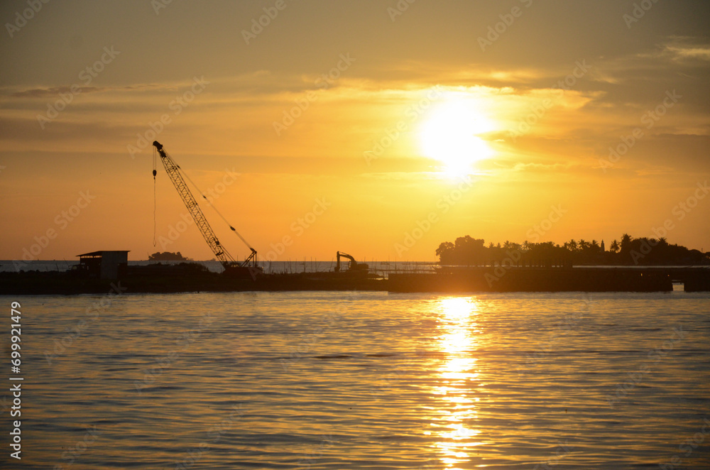 Silhouette construction boat and cranes setting in marine area to contract export pipeline business under to sea with beautiful sunset sky background.