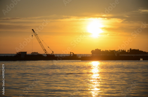 Silhouette construction boat and cranes setting in marine area to contract export pipeline business under to sea with beautiful sunset sky background.