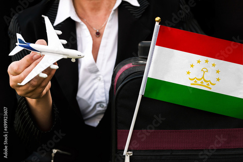 business woman holds toy plane travel bag and flag of Tajikistan 