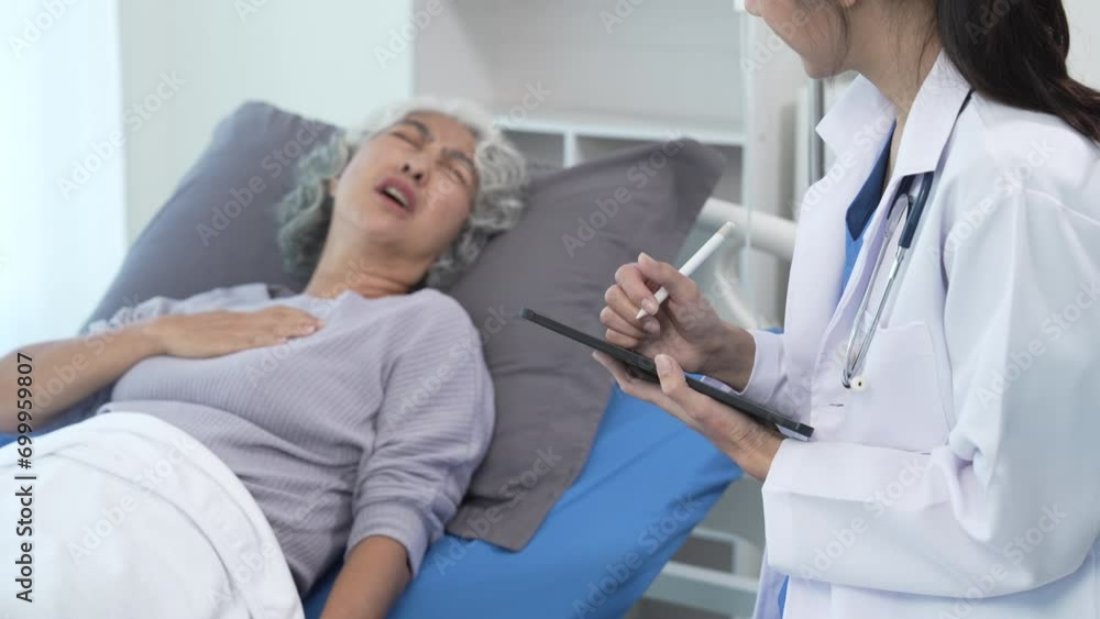 Elderly Asian woman lying in hospital bed looking unwell, with young Asian doctor take a history of illness Health check and encouragement. Elderly Asian woman lying in hospital bed looking unwell, with young Asian doctor take a history of illness Health check and encouragement.
