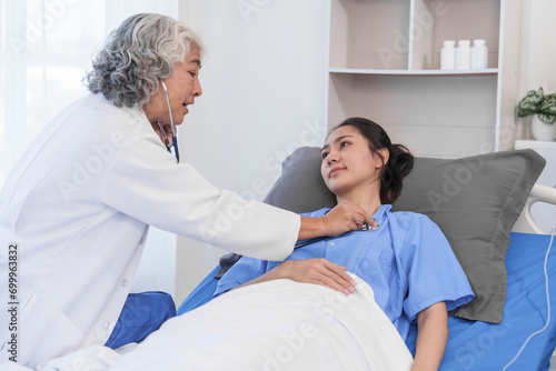 An elderly Asian doctor with a stethoscope is checking young Asian patient in hospital bed, take history of illness Health check and encouragement