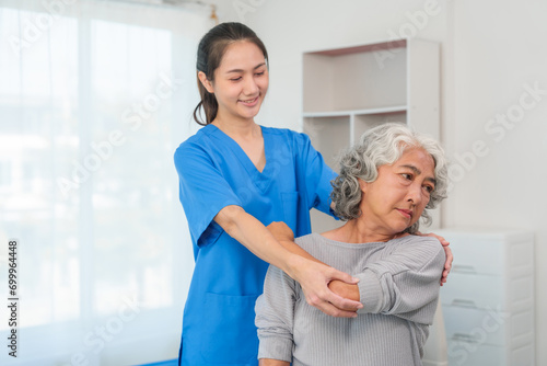 A young Asian nurse is assisting an elderly Asian woman with a grey hair during a physical therapy session. photo